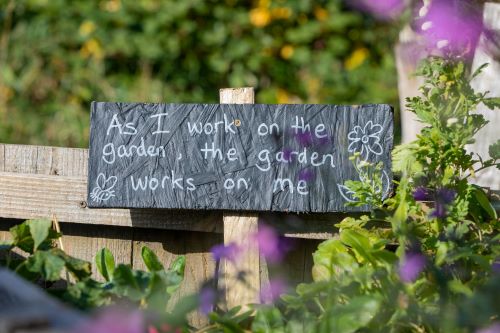  the picture of gardening, a sign reads: "As I work on the garden, the garden works on me."