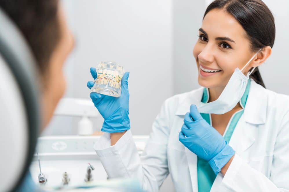An orthodontist showing a dental model with braces to a patient during a consultation.