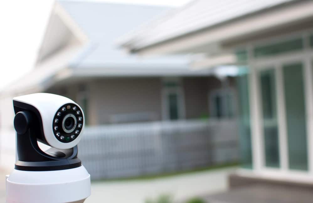 A security camera positioned outside a modern home with weatherboard cladding and green window frames.